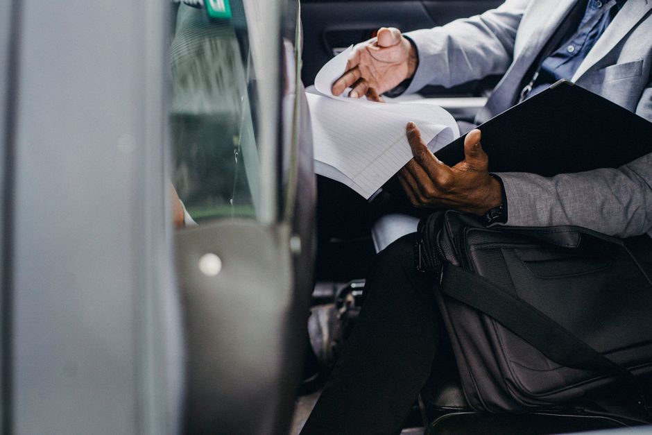 Busy crop anonymous African American male preparing important papers in folder while sitting in automobile