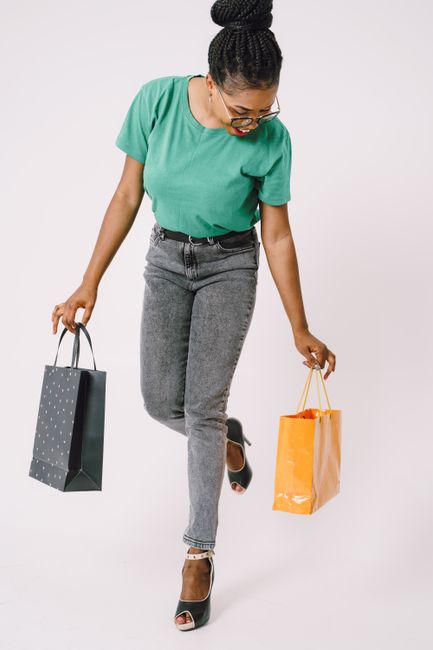 Stylish woman with shopping bags smiling in a studio on a white background, full of joy and fashion sense.