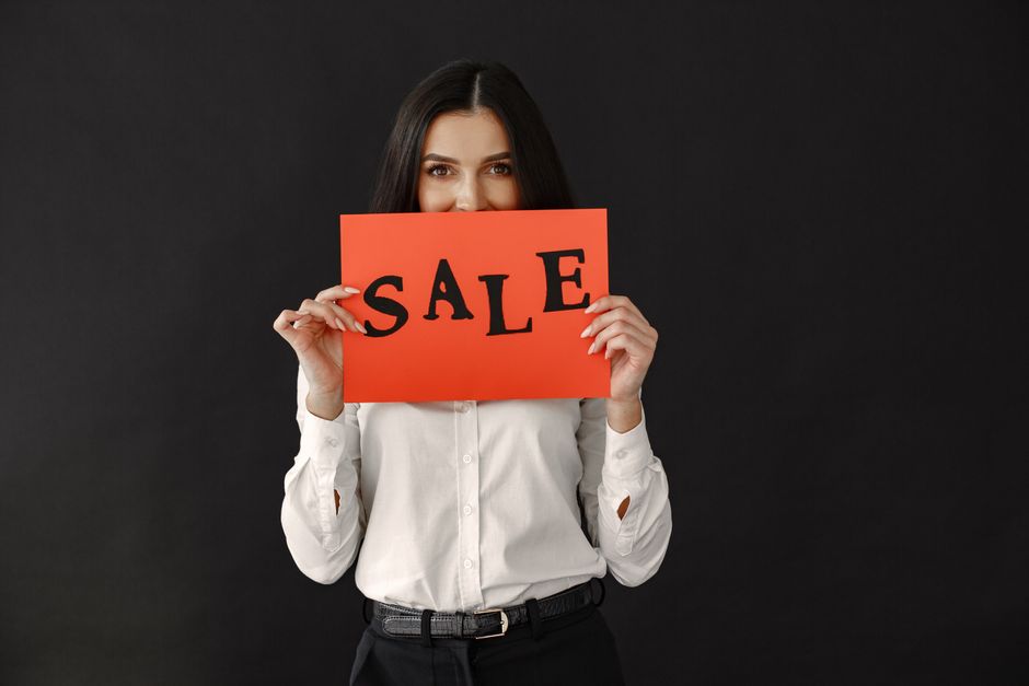 Woman in white shirt holding a red sale sign against a black backdrop. Ideal for advertising.